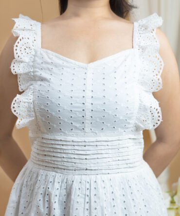 Close-up of white cotton eyelet dress showing lace hem, embroidery, and ruffle strap details