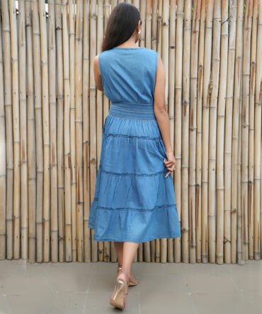 Back view of a denim blue sleeveless tiered midi dress with smocked waist