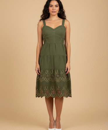 Model wearing olive green cotton midi dress with tan eyelet embroidery and tiered detailing.