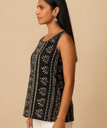 Model in side view wearing a black batik print sleeveless kurti with scoop neckline and white pants.