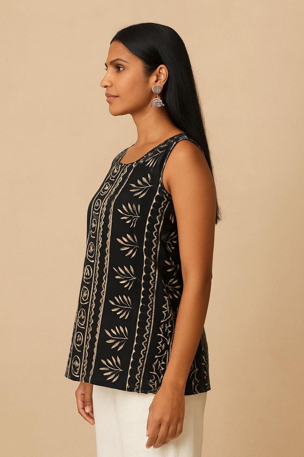 Model in side view wearing a black batik print sleeveless kurti with scoop neckline and white pants.