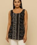 Model wearing a sleeveless black batik print kurti with scoop neckline and white pants, front view.