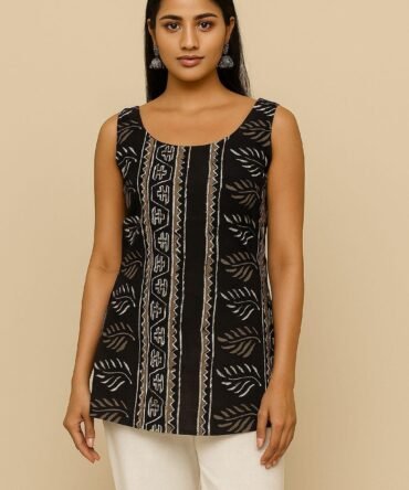 Model wearing a sleeveless black batik print kurti with scoop neckline and white pants, front view.