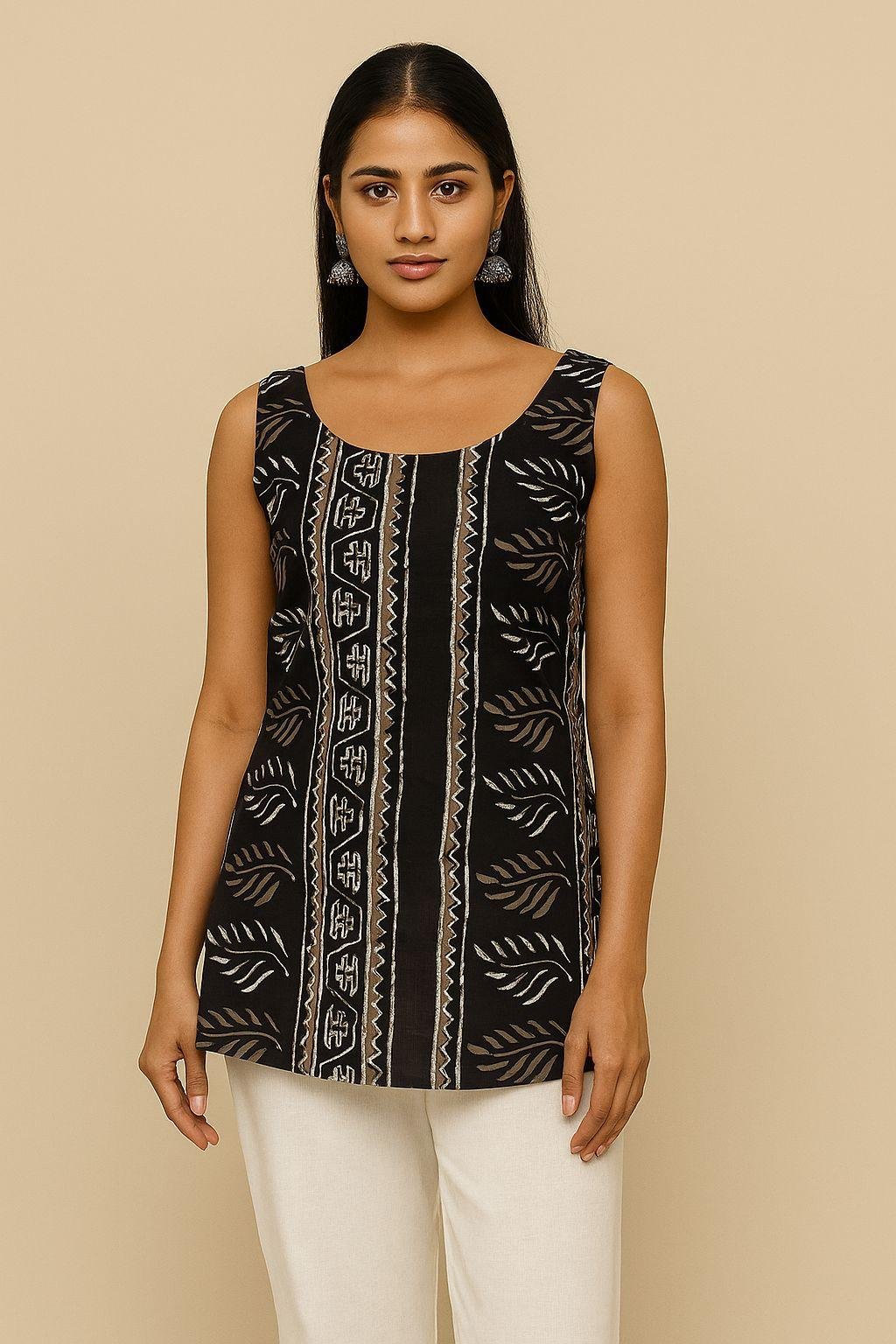 Model wearing a sleeveless black batik print kurti with scoop neckline and white pants, front view.